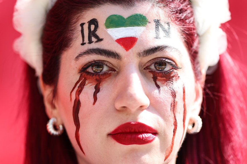 A woman wearing make-up that looks like she is crying tears of blood with IRAN across her forehead.
