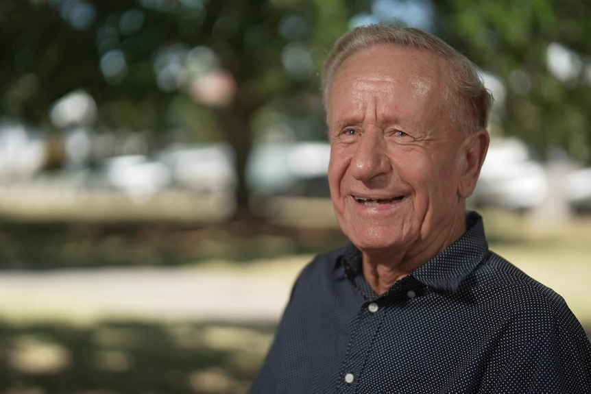 An eldrly man smiling - outdoor background is blurred. 