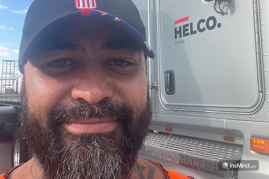 A man taking a selfie in front of truck with a cap on.