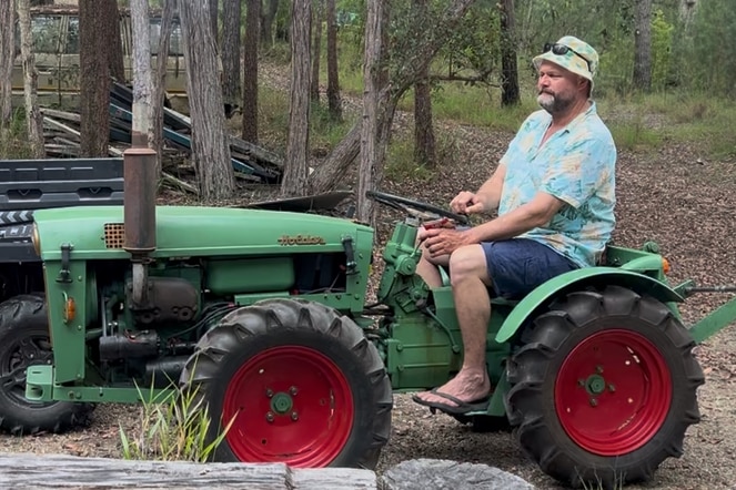 A man in a Hawaiian shirt riding a green tractor.