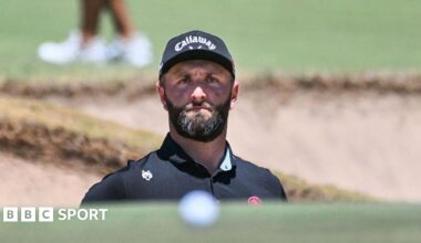Jon Rahm playing from a bunker. His ball is in the foreground of the image.