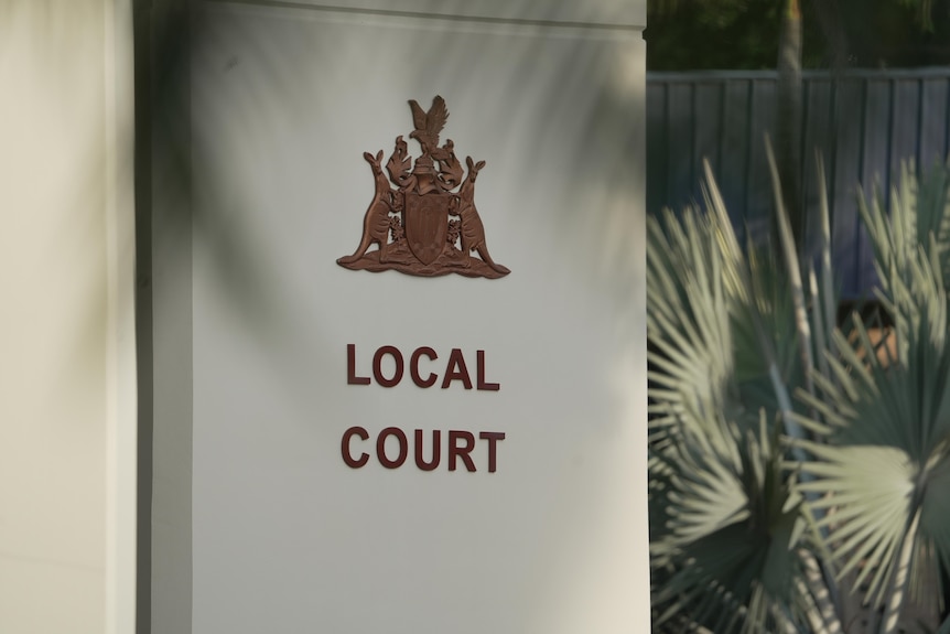 A flat white column at the front of a building with a coat of arms and the words "Local Court" written on it.