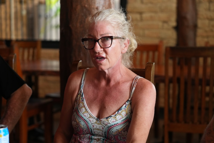 A woman in black framed glasses, multi-coloured and pattern singlet derss, sitting on wooden chair
