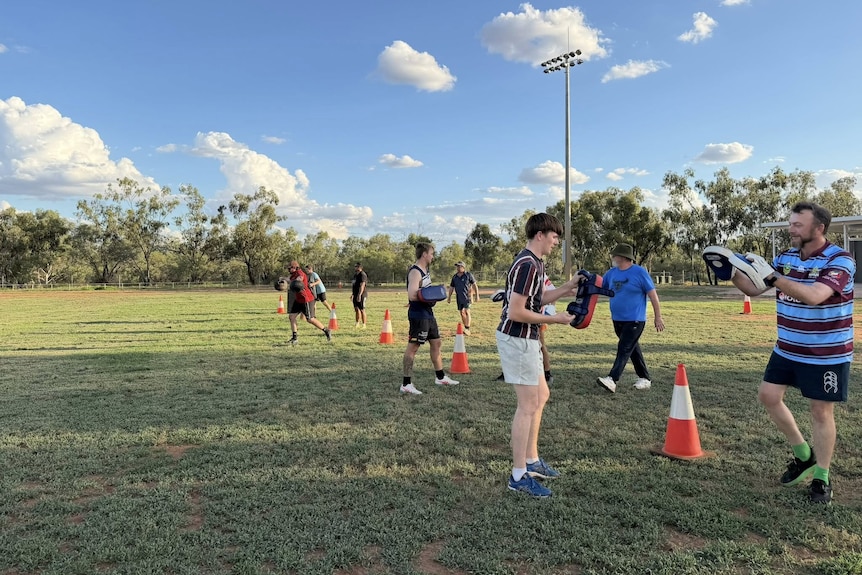 Two lines of people standing on green oval with boxing gloves. 