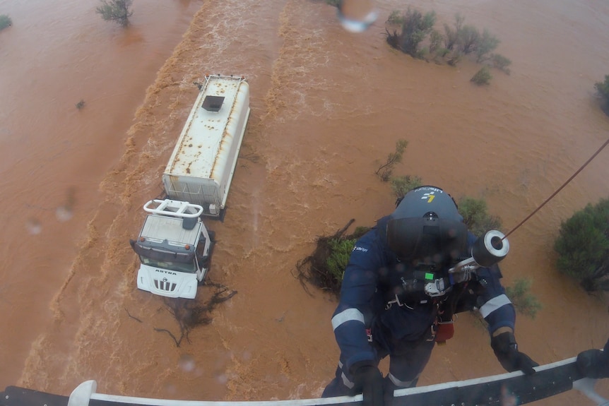 A view of a truck in the middle of brown water with a rescue being lowered toward the truck
