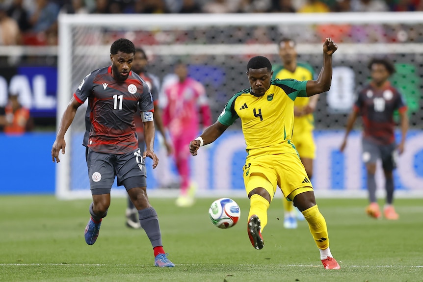 A member of Jamaica's national men's football team kicks the ball as a defender chases