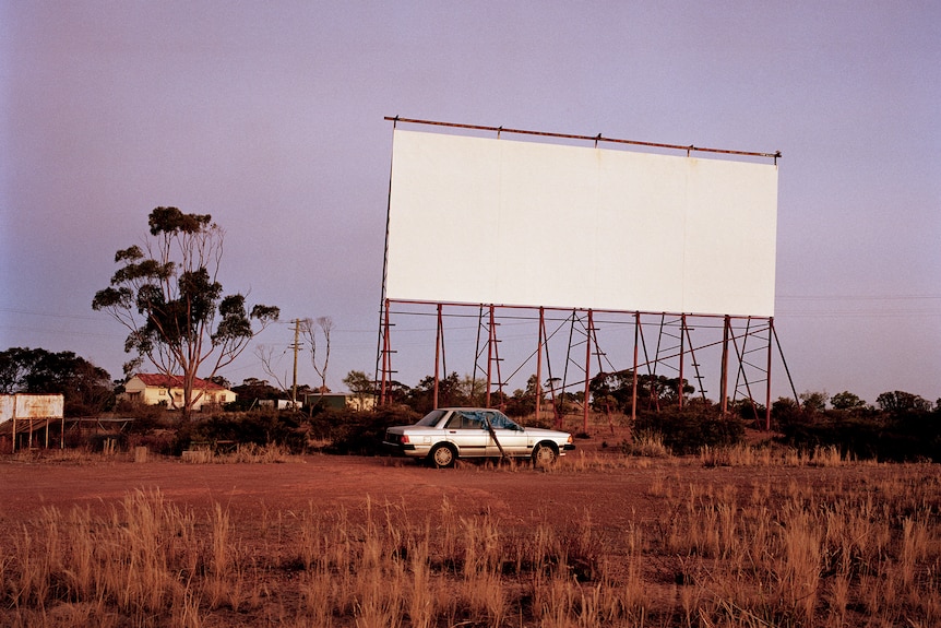 A blank white drive-in screen in front of a dark purple sky