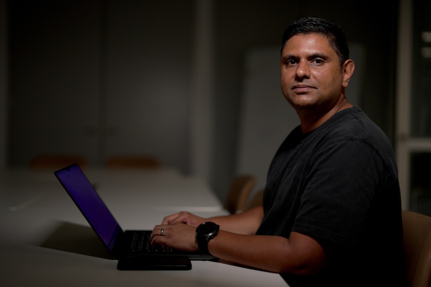 A man sitting at a desk with a laptop in front of him.