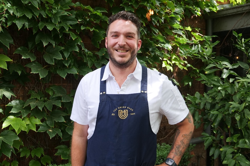 Man stands in front of a wall of greenery.
