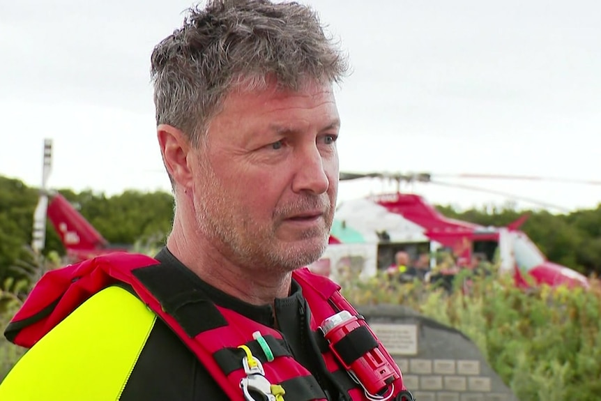 A paramedic in lifejacket with a rescue helicopter in the background