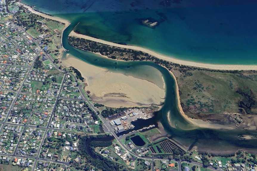 A satellite view of a sandy channel leading to the ocean, near a city.