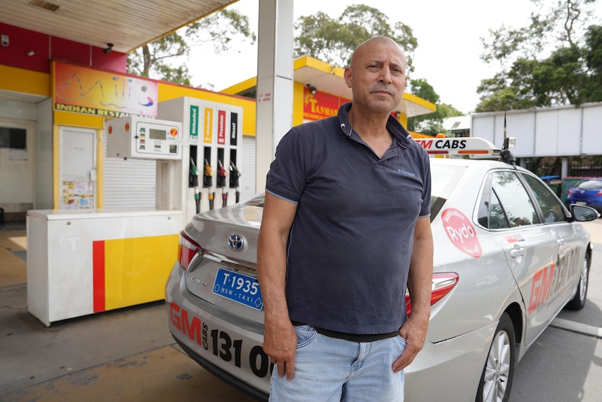 Frank stands behind a taxi parked at a service station, looking concerned.