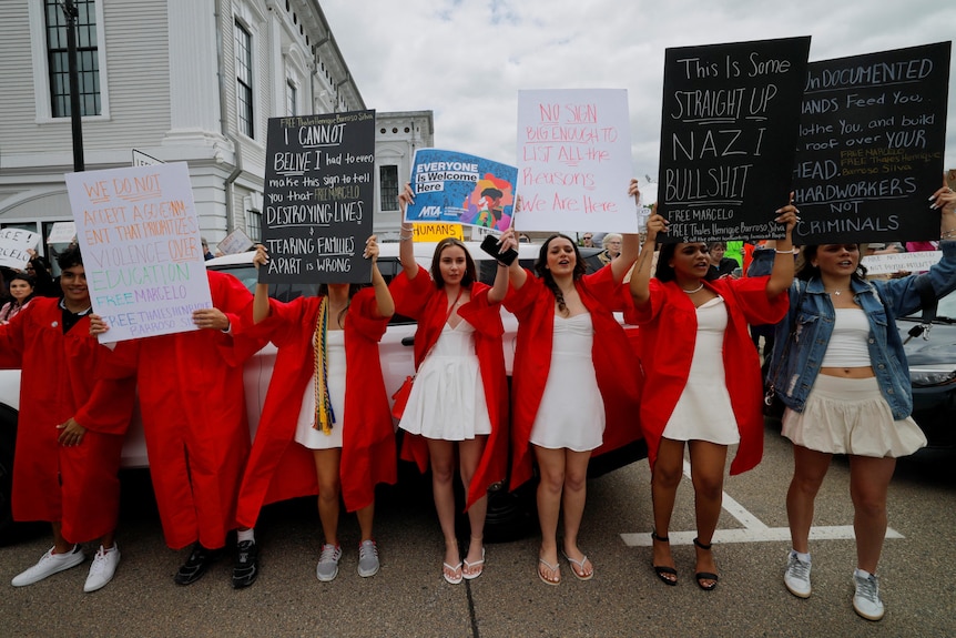 Teenagers in red gowns hold protest signs