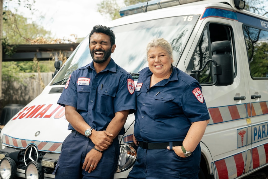 Nazeem Hussain and Urzila Carlson are dressed as paramedics in front of an ambulance. Nazeem is laughing with eyes closed