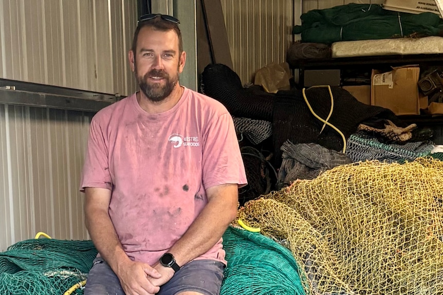 A young man with a beard sitting on fishing nets.
