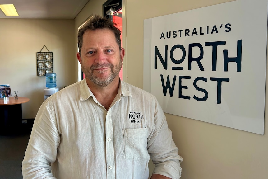 A man in a white shirt smiles in front of a sign that says "Australia's North West".