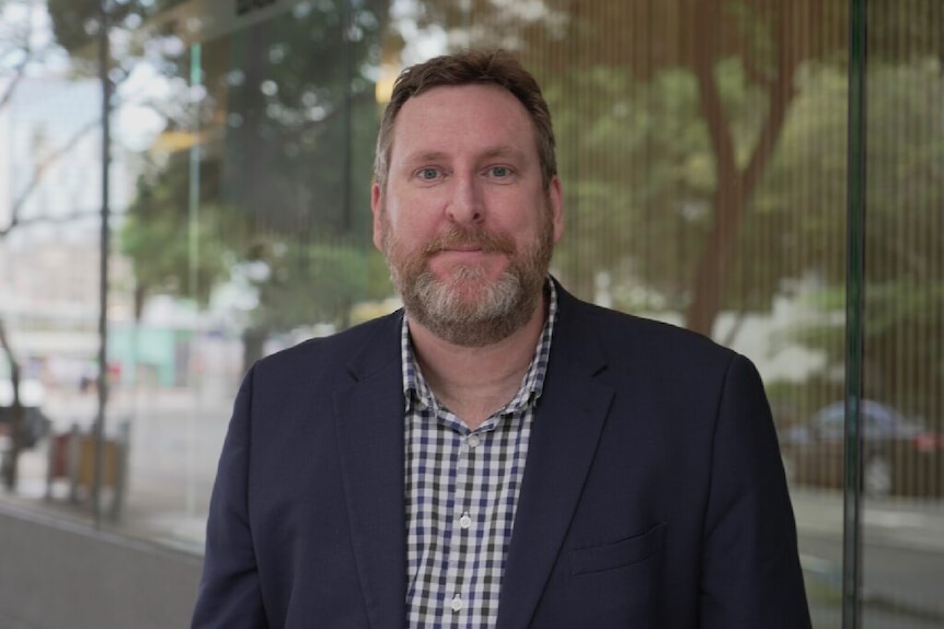 Man with beard in shirt and jacket smiles with mouth closed 