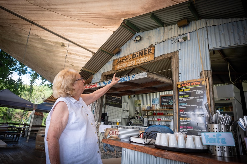 A woman in white points to a marker on the side of a building