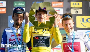 Jonas Vingegaard holds the Paris-Nice trophy in front of his face and stands next to Dani Martinez and Georg Steinhauser