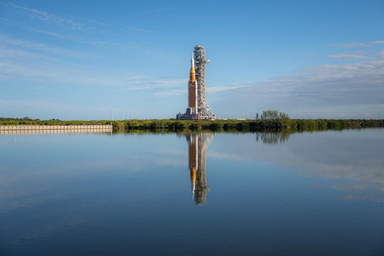 A rocket on a launchpad overlooking water.