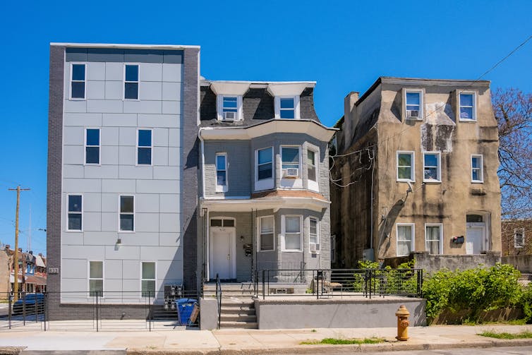 View of grey, boxy new construction building next to two older, more traditional houses