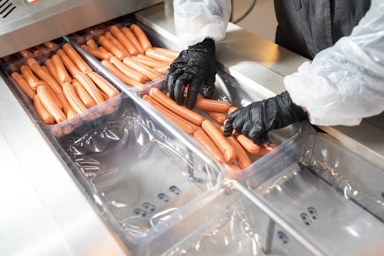 A factory worker putting sausages in a container.