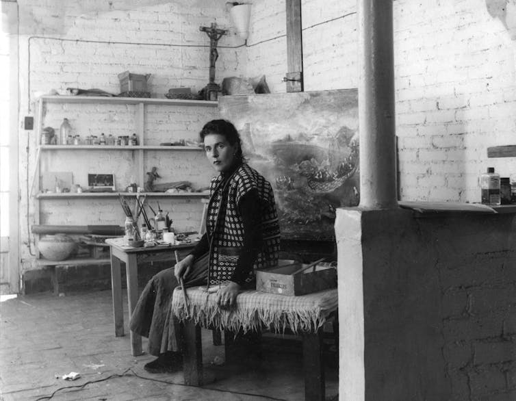 Leonora Carrington sitting in her studio in front of a large easel
