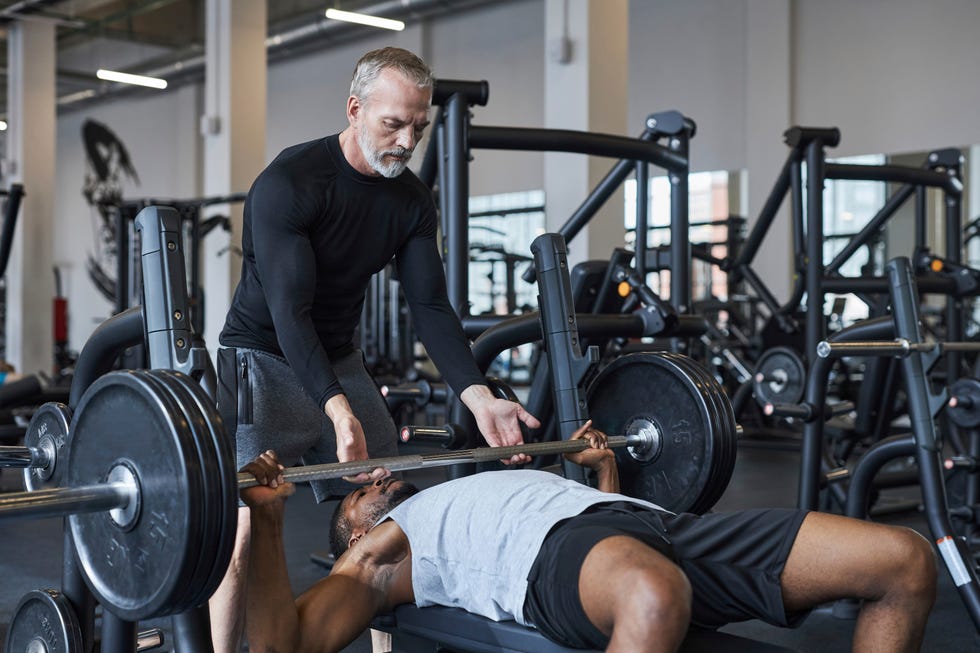 fitness instructor helping young man with bench press in gym