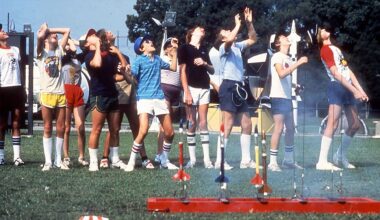 kids in multi-color t-shirts and shorts watch model rockets fly as other rockets stand ready to fly from a launch pad