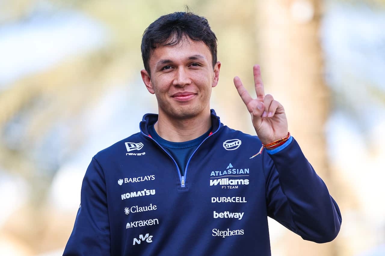 A man wearing a blue jumper giving a peace sign to a camera.