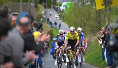Riders approach on a narrow road with spectators on either side of the road