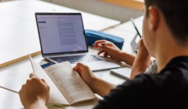 A student points at a computer screen while writing.