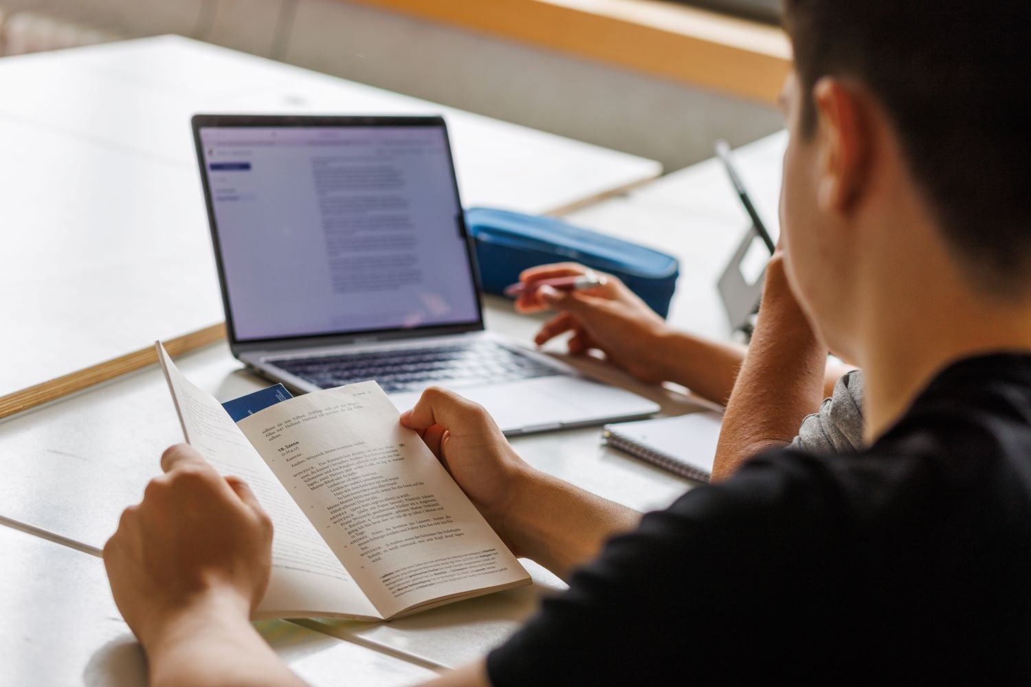 A student points at a computer screen while writing.