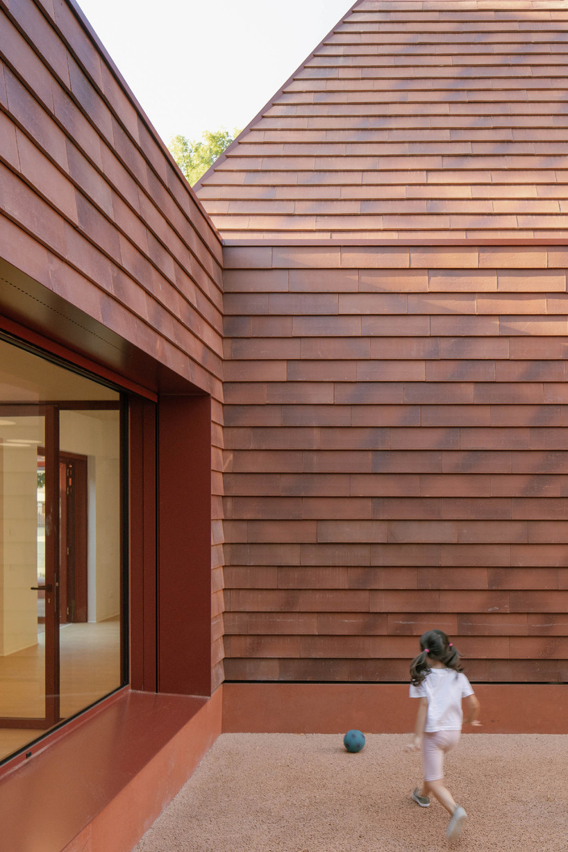 a cluster of terracotta-tiled pyramidal houses envelopes kindergarten in italy - 8
