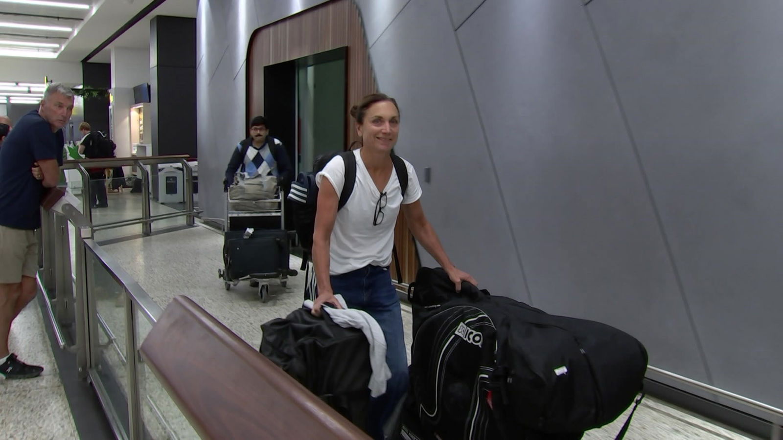 A woman walks through an airport with lots of luggage