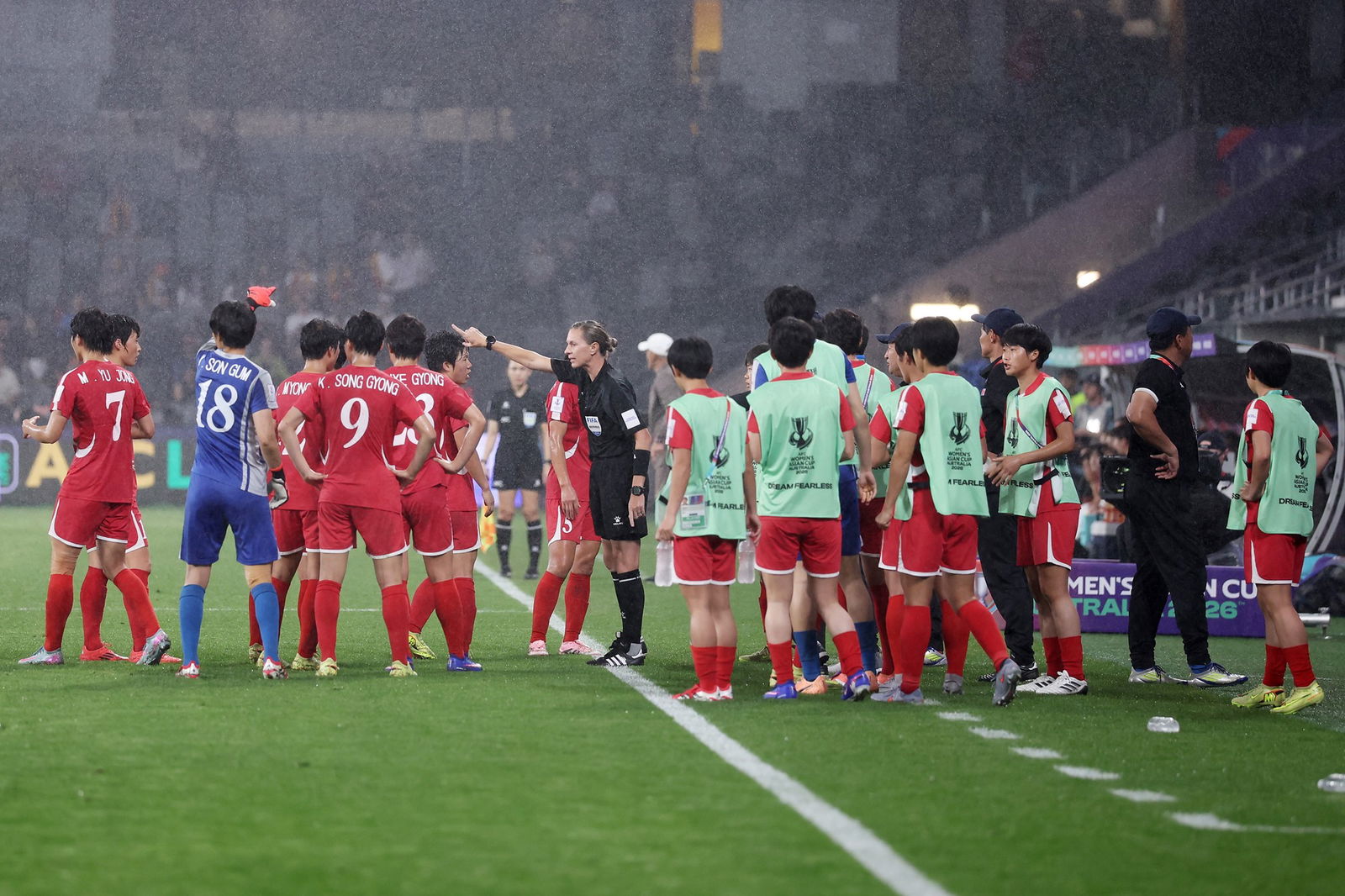 A group of players stand in pouring rain arguing with a referee