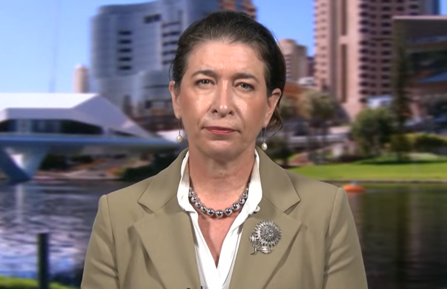 A middle-aged woman sits in front of a backdrop showing Adelaide's CBD.