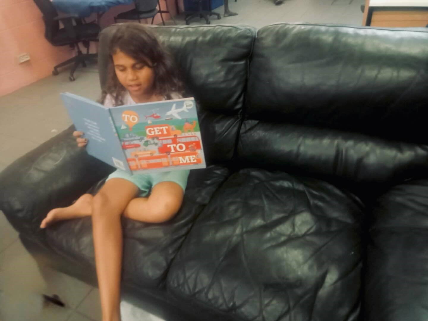A girl sitting on a leather couch reading a picture book