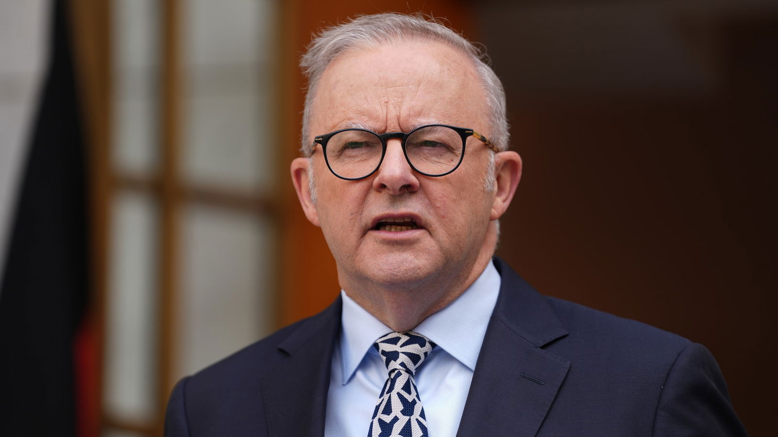 A close up of Anthony Albanese speaking in a suit, tie and glasses