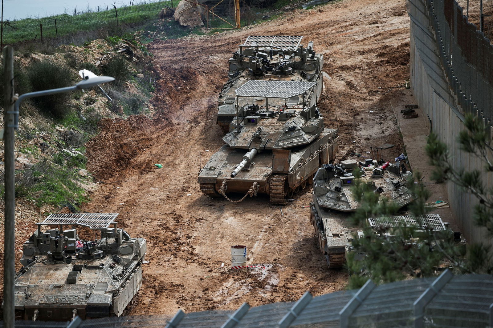Army vehicles driving on a dirt road near a fence