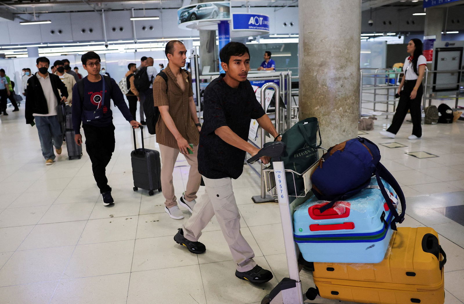 One rescued sailor pushes a trolly with his luggage, followed by others. 