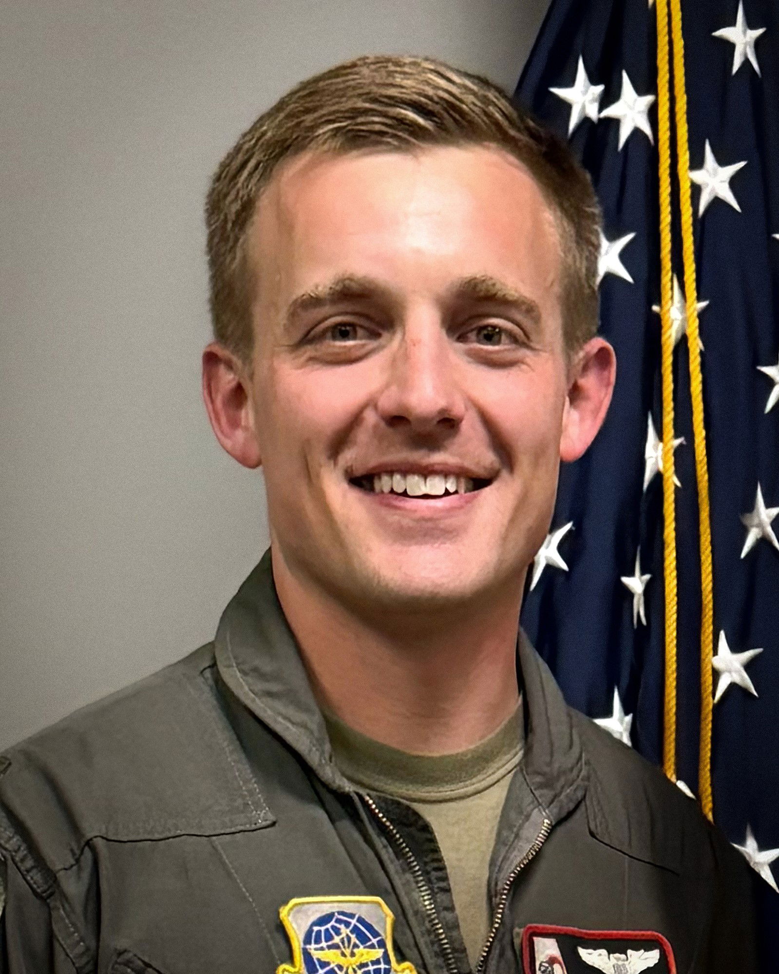 A soldier's headshot, a man in uniform smiles in front of US flag