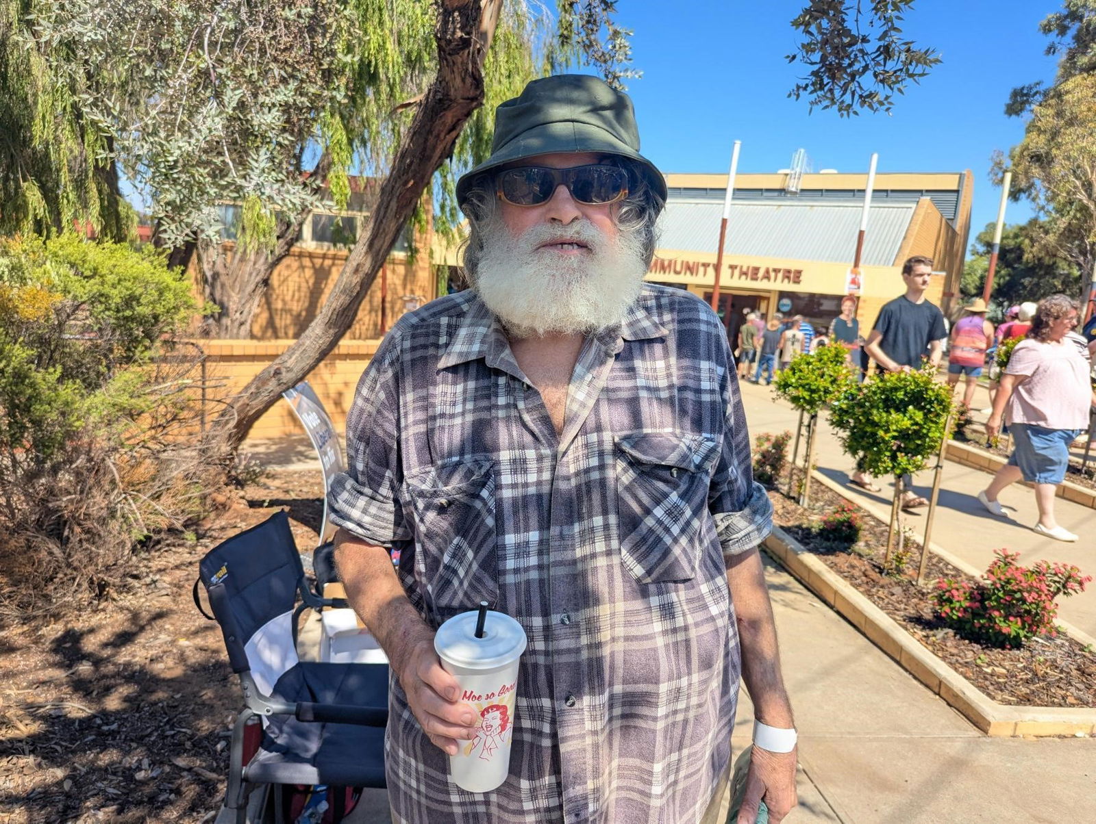 A man with a beard wearing sunnies and a hat looks at the camera