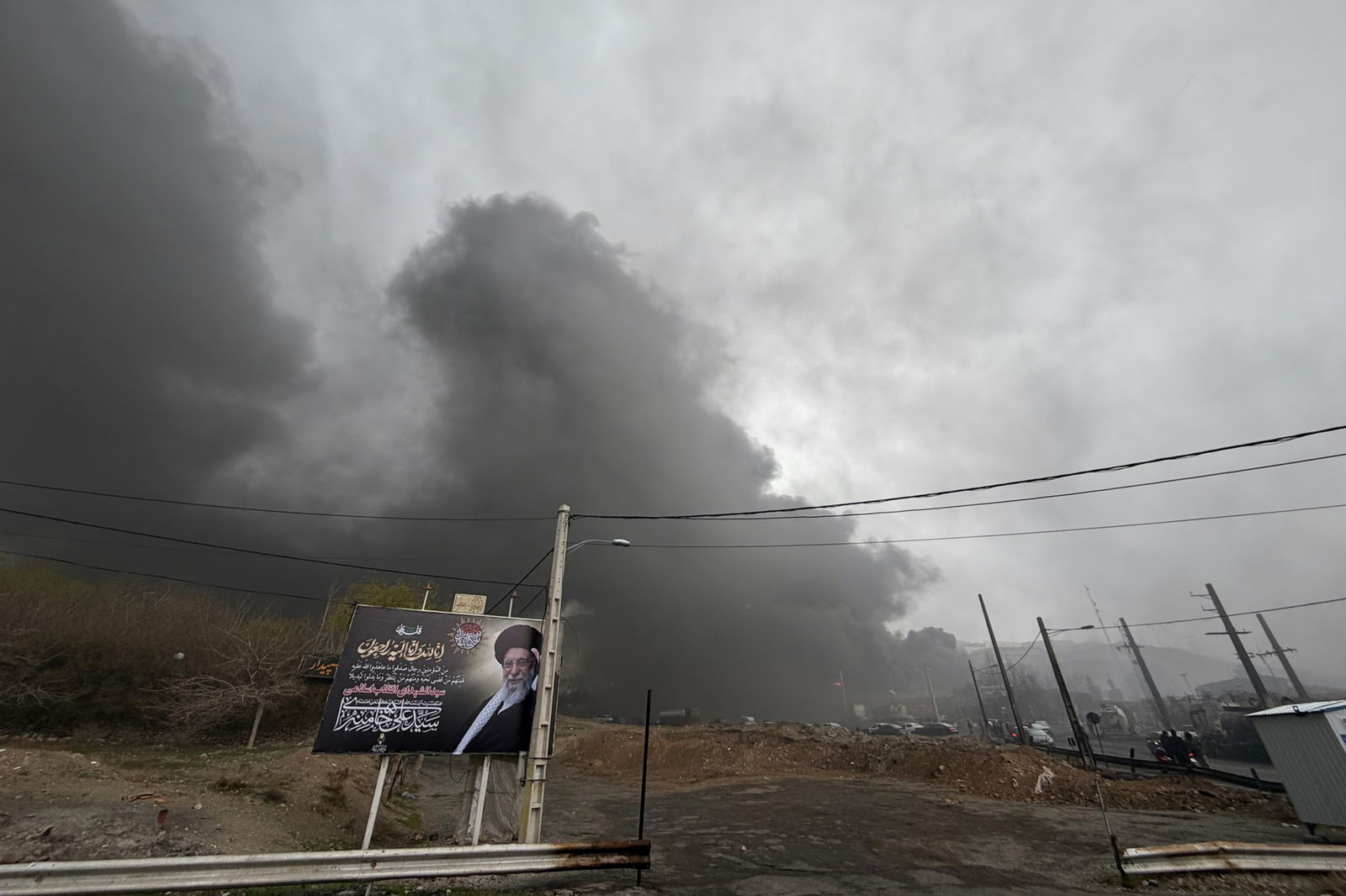 Thick smoke hangs in a grey sky over an oil facilty. 