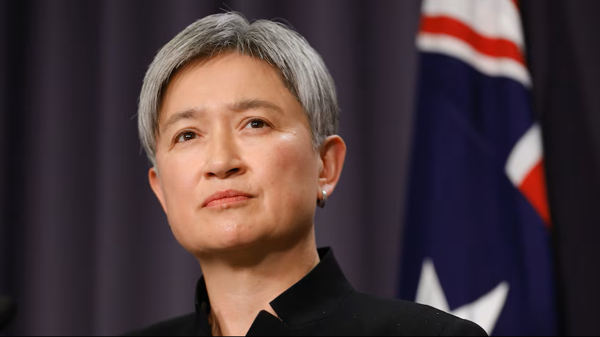 Penny Wong looks serious in front of an Australian flag.