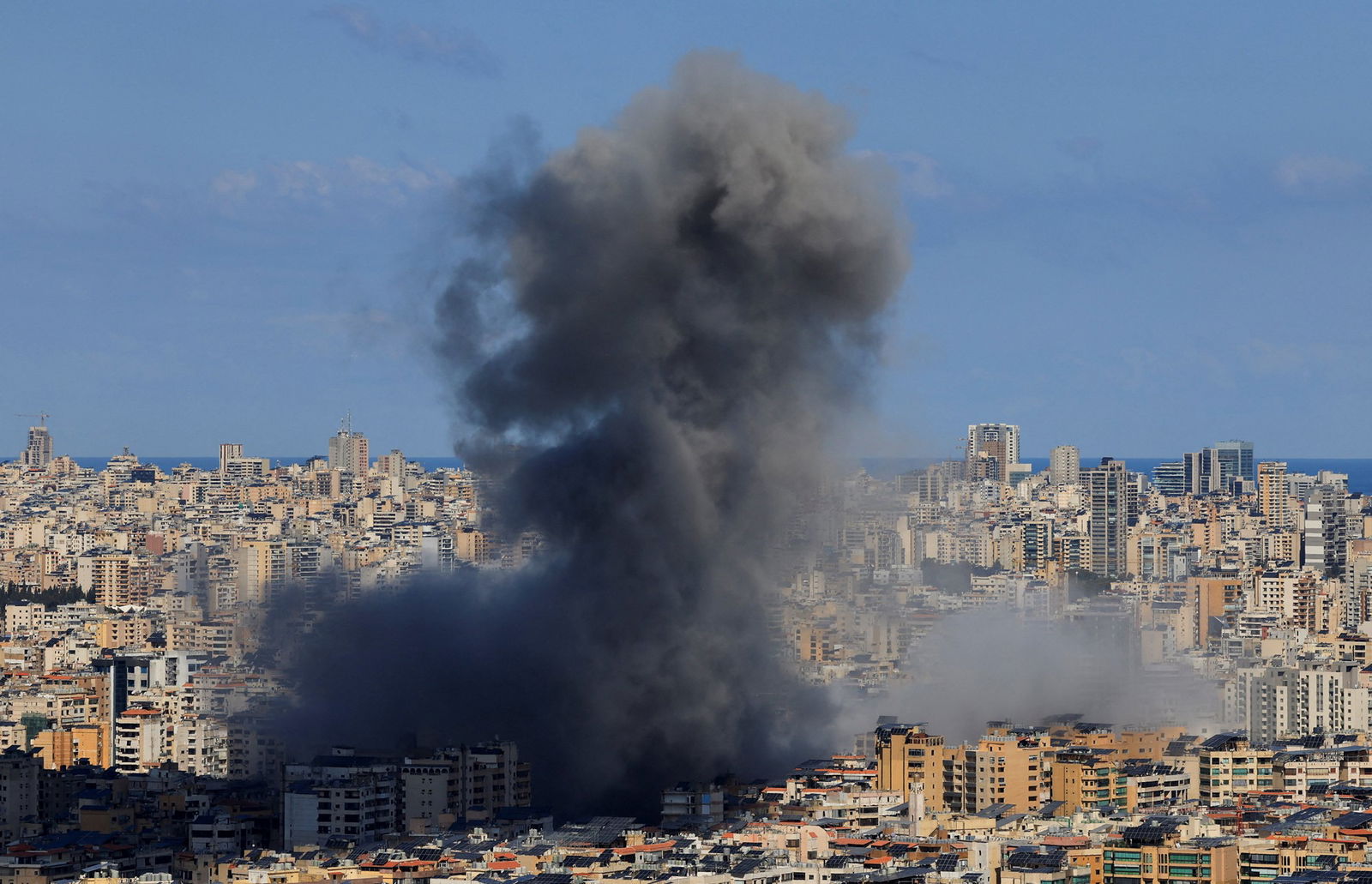 a dark smoke cloud plooms from a city 
