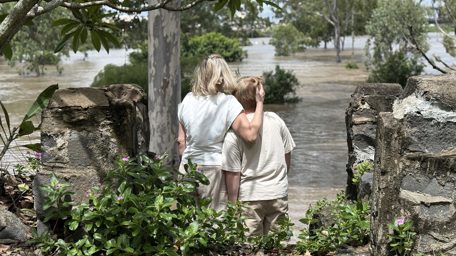 a mum and son face away from the camera looking at rising river levels