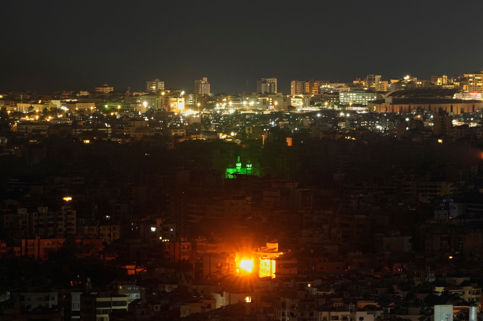 a fireball at night bursts out of an apartment building, with the city skyline in back 