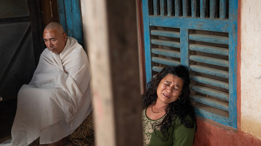A man and woman sit on the floor of a mud-brick home.