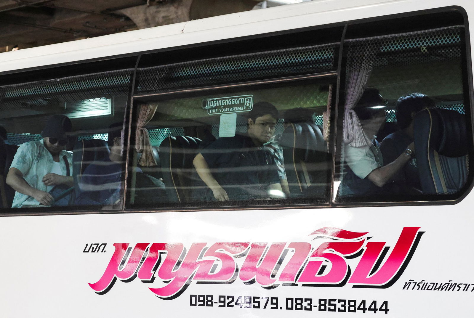 The crew members on a bus with Thai words written in pink on the side. 